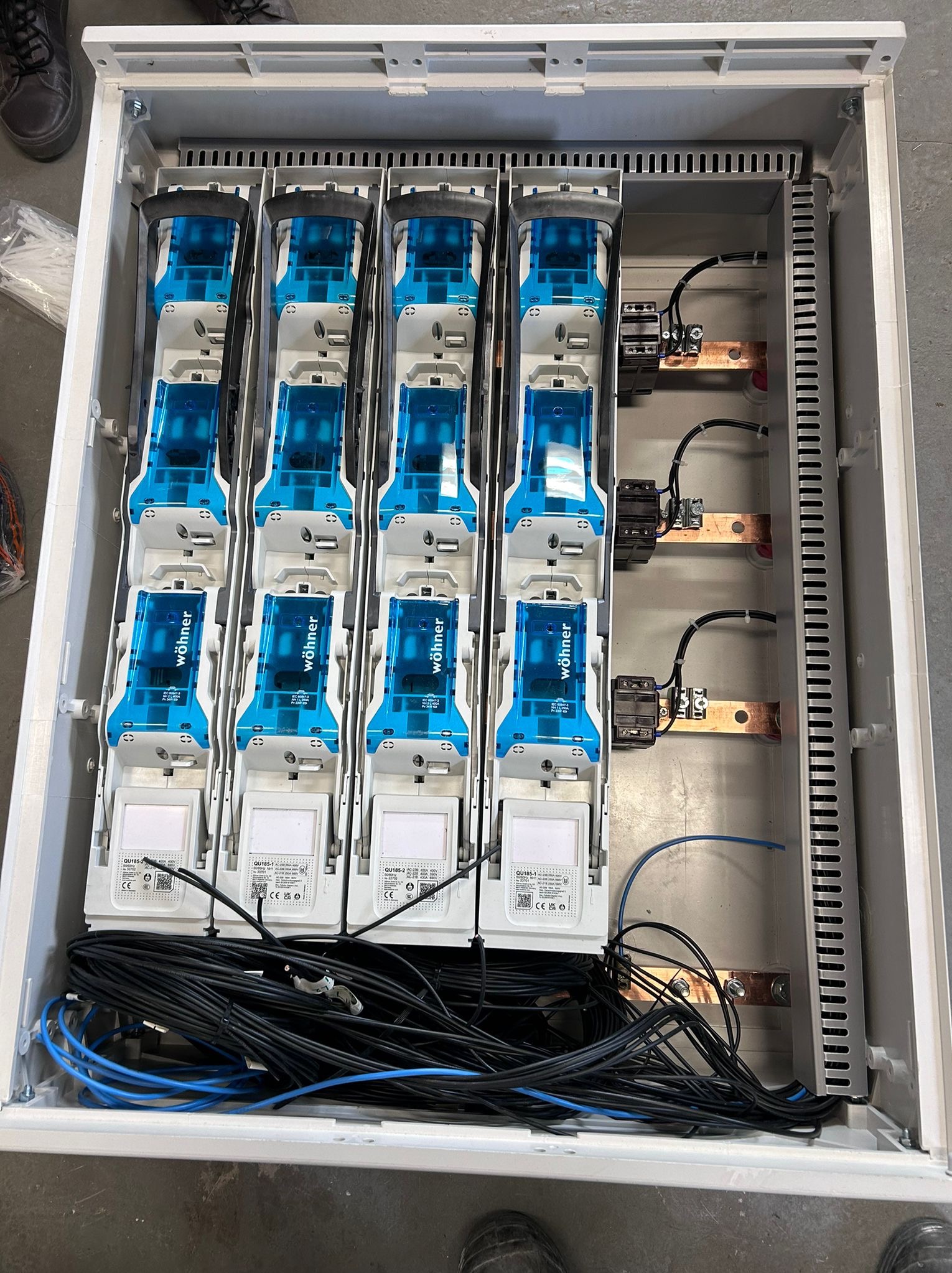 Rozdzielnica elektryczna z modułami Wöhner, widok z góry. Widoczne przewody, szyny miedziane i elementy zabezpieczające. Biała obudowa z szarym tłem.