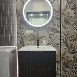 Lucas - Nowoczesna łazienka: umywalka z szafką w kolorze ciemnego drewna, okrągłe lustro z podświetleniem LED i płytki w tropikalne wzory. Minimalistyczny design.