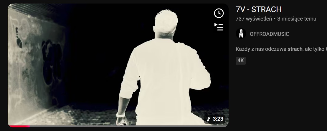 Kadr z teledysku: postać w jasnej koszuli idzie w ciemnym tunelu z graffiti, widok z tyłu, obok informacje o utworze i wykonawcy.