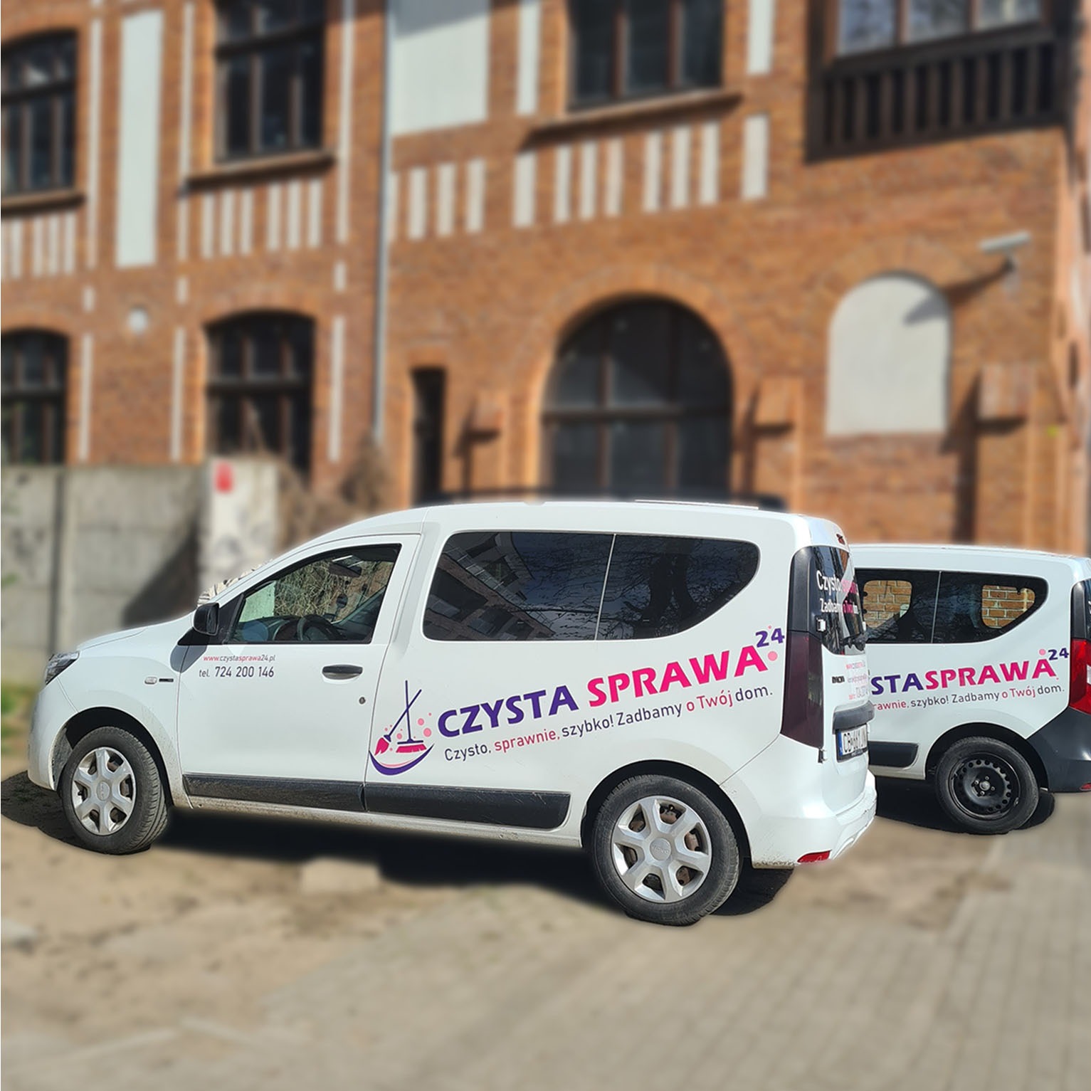 Dwa białe busy firmy sprzątającej 'Czysta Sprawa 24' zaparkowane przed budynkiem z cegły. Na busach widoczne logo firmy i numer telefonu.