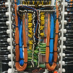 Sławomir Troszczynski - Rozdzielnica elektryczna z uporządkowanymi kablami w kolorach: brązowym, niebieskim i zielono-żółtym. Widoczne narzędzia: obcinaczki, szczypce i śrubokręt.