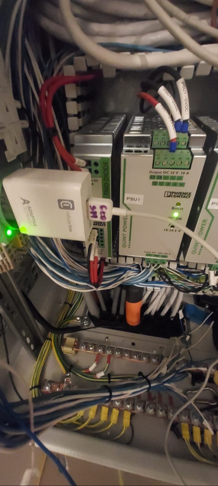 Szafa sterownicza z modułami zasilania Phoenix Contact Quint Power, adapterem Cellularline i okablowaniem. Widoczne złącza, przewody i oznaczenia na urządzeniach.