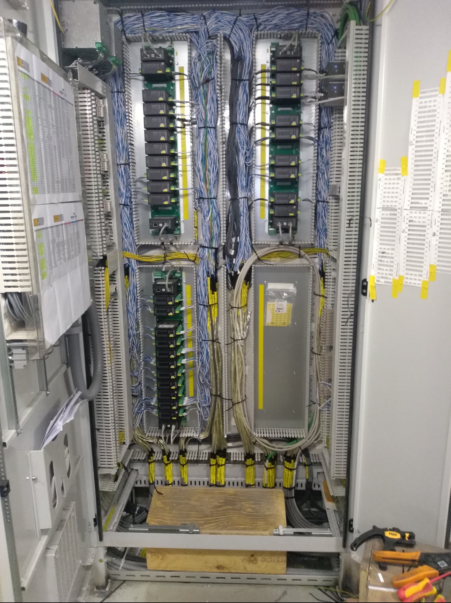 Rozbudowana szafa sterownicza z precyzyjnie ułożonymi kablami, modułami elektronicznymi i listwami zaciskowymi. Widoczne narzędzia elektryczne sugerują etap prac instalacyjnych.