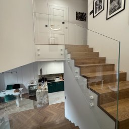 Szkłomania Piotr Błaszczyk - Nowoczesne schody z drewnianymi stopniami i szklaną balustradą, widok z góry, jasne wnętrze z elementami wystroju.
