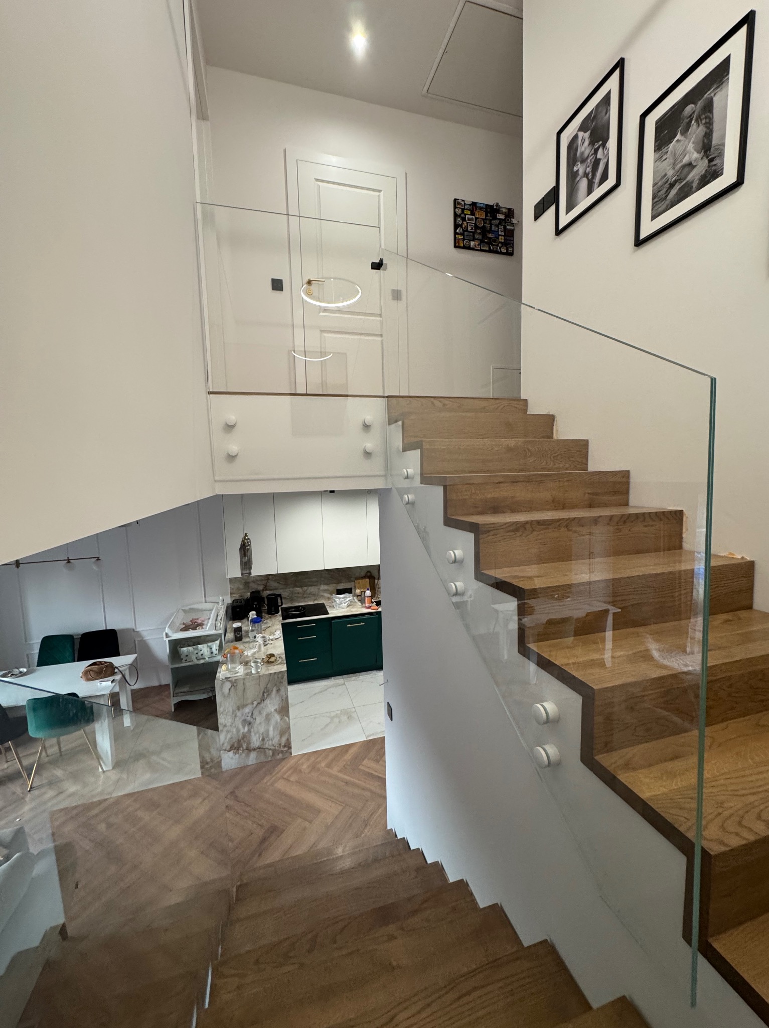 Nowoczesne schody z drewnianymi stopniami i szklaną balustradą, widok z góry, jasne wnętrze z elementami wystroju.