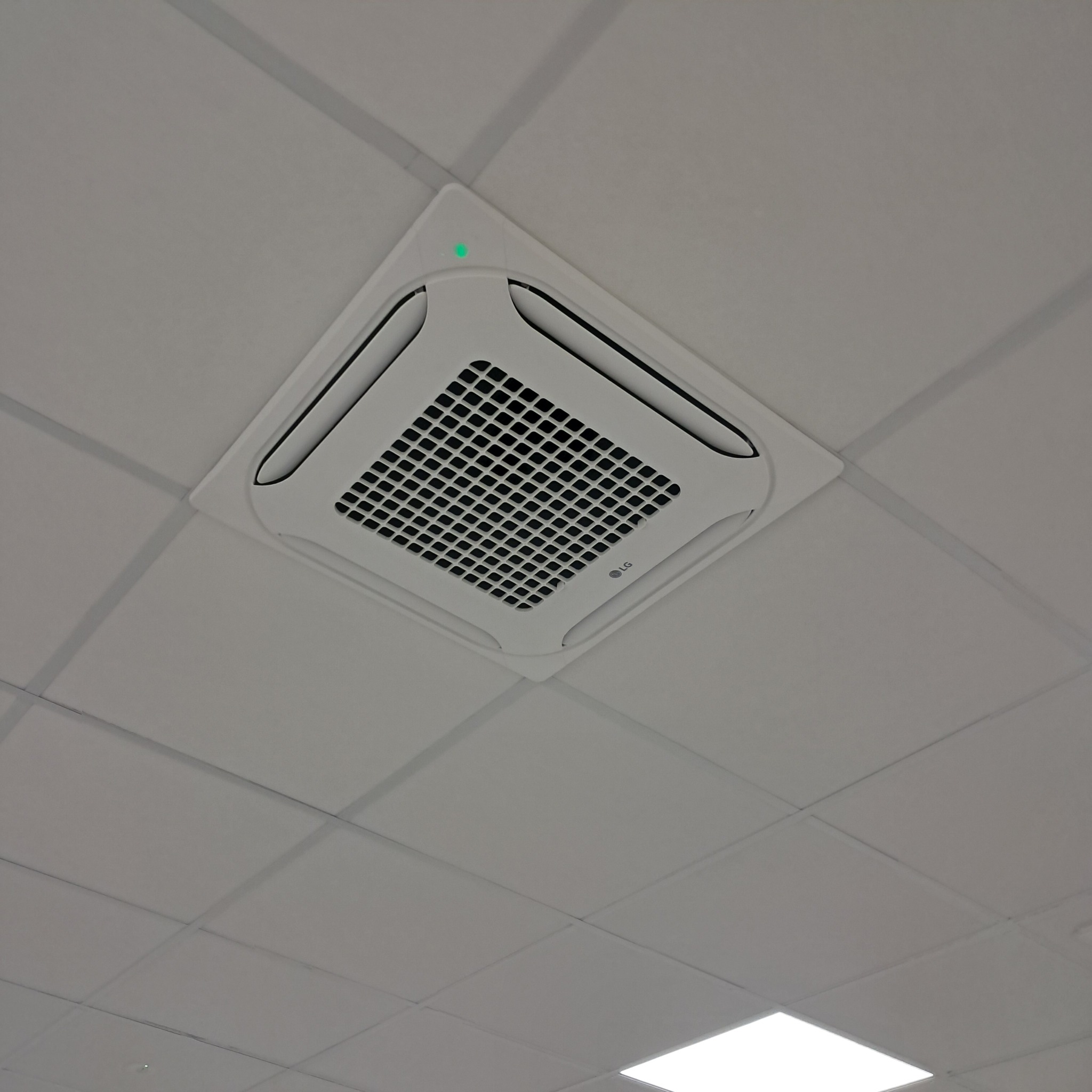 Kasetonowa klimatyzacja LG zamontowana w suficie podwieszanym z widoczną zieloną diodą sygnalizacyjną. Ujęcie z dołu.