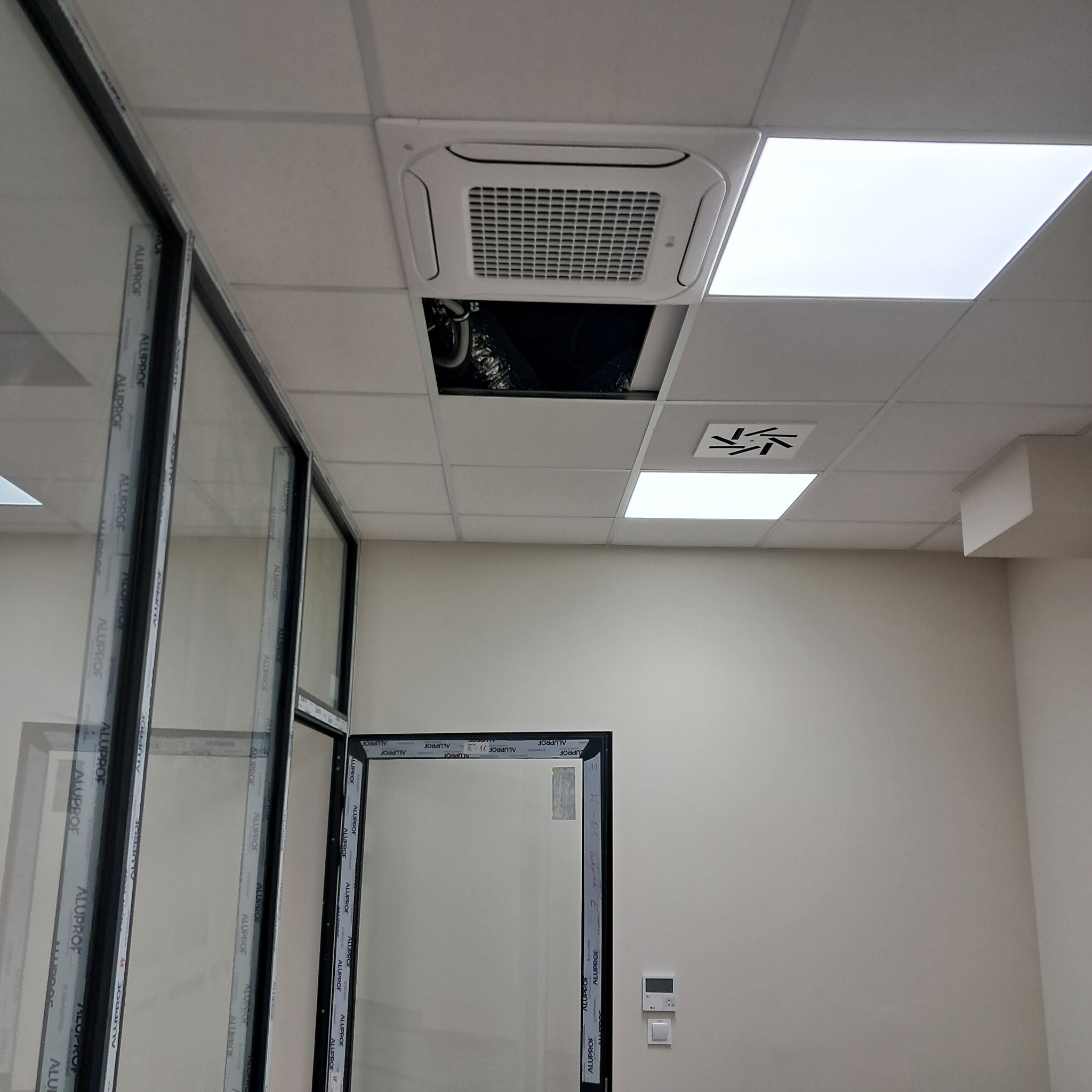 Montaż sufitowej klimatyzacji kasetonowej w biurze w Lubinie. Widoczne otwarte panele sufitowe i instalacja. Nowoczesne, przeszklone biuro.