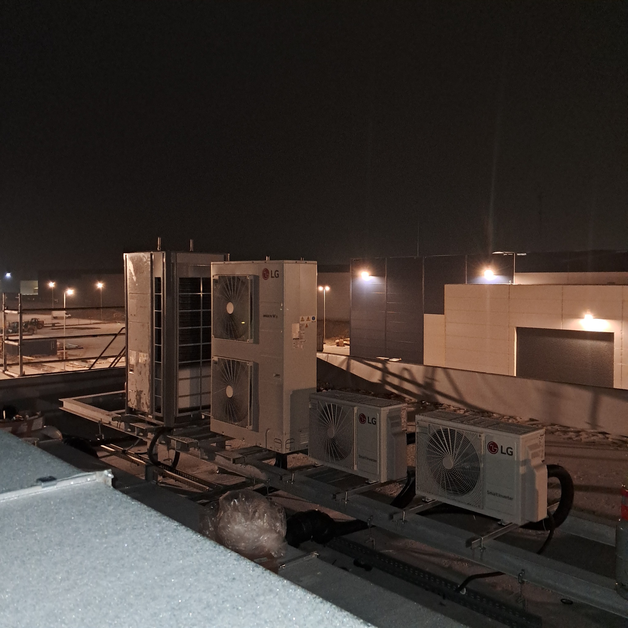 Instalacja klimatyzacji LG na dachu budynku biurowego nocą. Widoczne jednostki zewnętrzne, metalowa konstrukcja wsporcza i oświetlenie zewnętrzne.