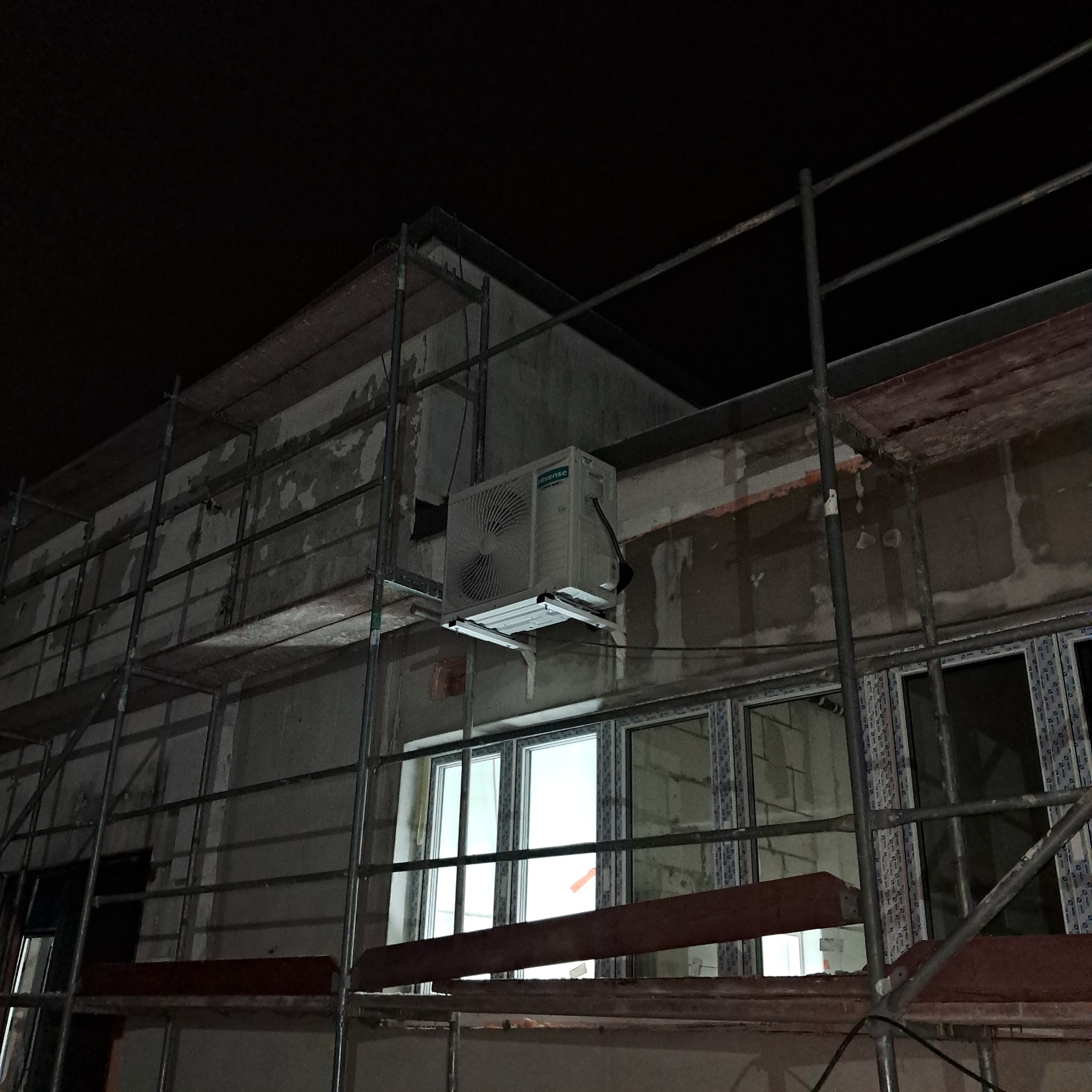 Zewnętrzna jednostka klimatyzacji Hisense zamontowana na elewacji budynku w trakcie remontu, widoczna z rusztowania. Nocne ujęcie.