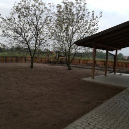 IZO-BAU Piotr Powroźnik - Przygotowany teren pod budowę z widoczną, kolorową, drewnianą palisadą, wykopem i zadaszeniem. W tle drzewa i pochmurne niebo.