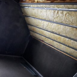 B.W.I.P. SPÓŁKA Z OGRANICZONĄ ODPOWIEDZIALNOŚCIĄ - Ocieplenie poddasza wełną mineralną, widoczne metalowe profile i czarna folia paroizolacyjna. Ujęcie z dołu, ukazujące strukturę izolacji i elementy konstrukcyjne.