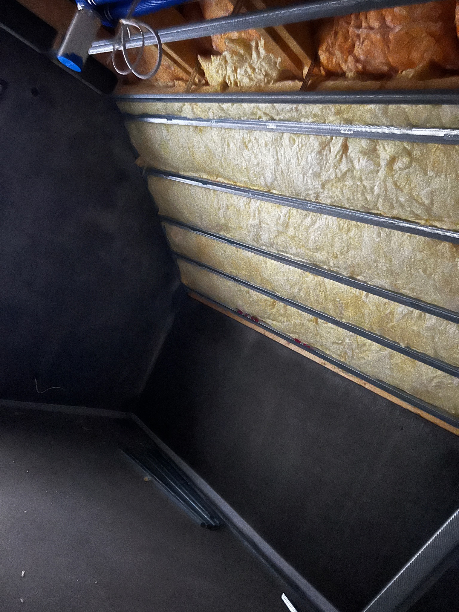 Ocieplenie poddasza wełną mineralną, widoczne metalowe profile i czarna folia paroizolacyjna. Ujęcie z dołu, ukazujące strukturę izolacji i elementy konstrukcyjne.