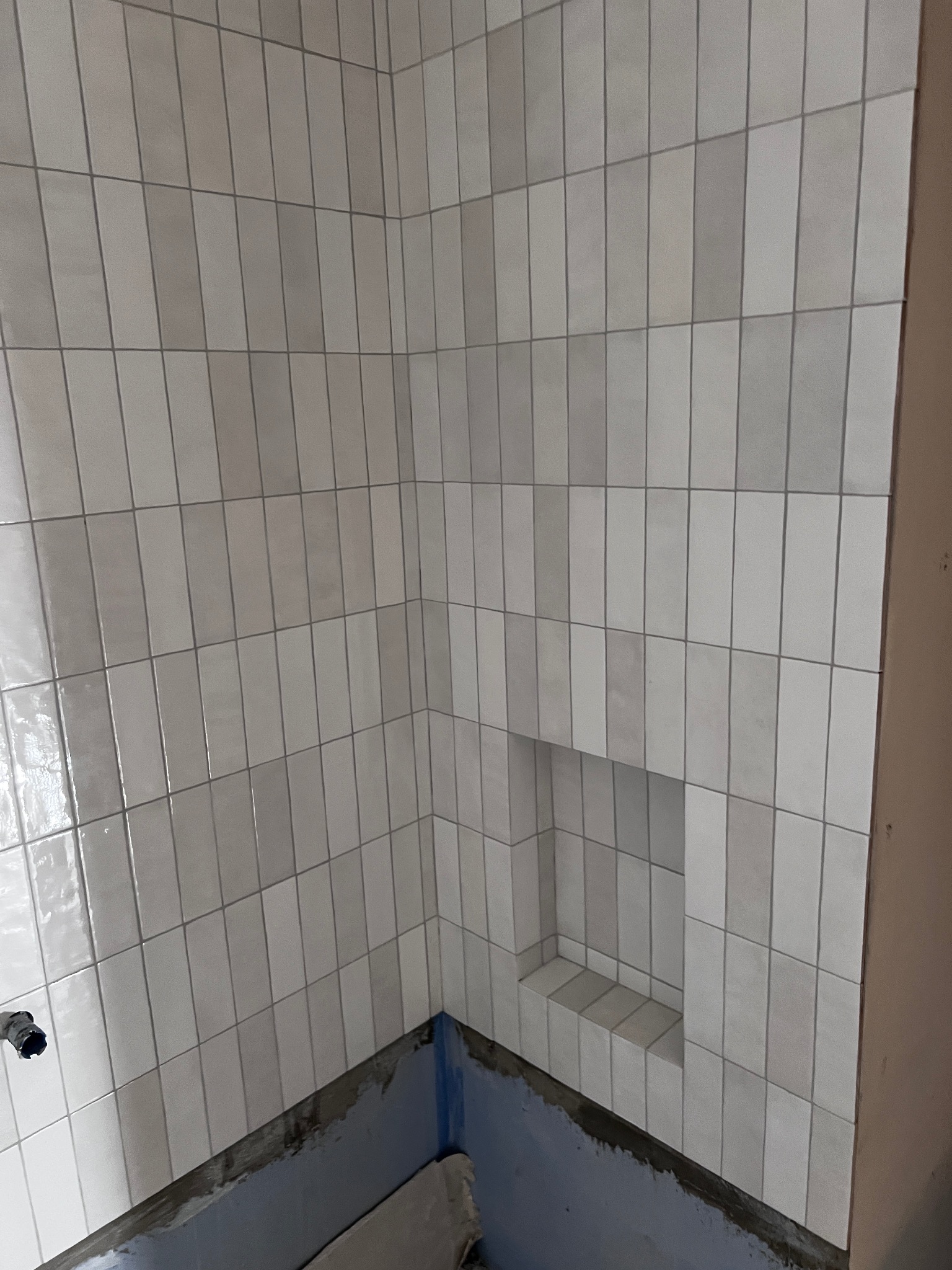 Ułożone pionowo, podłużne, białe płytki w łazience we Wrześni. W ścianie wnęka wyłożona tymi samymi płytkami. Widoczny fragment brodzika.