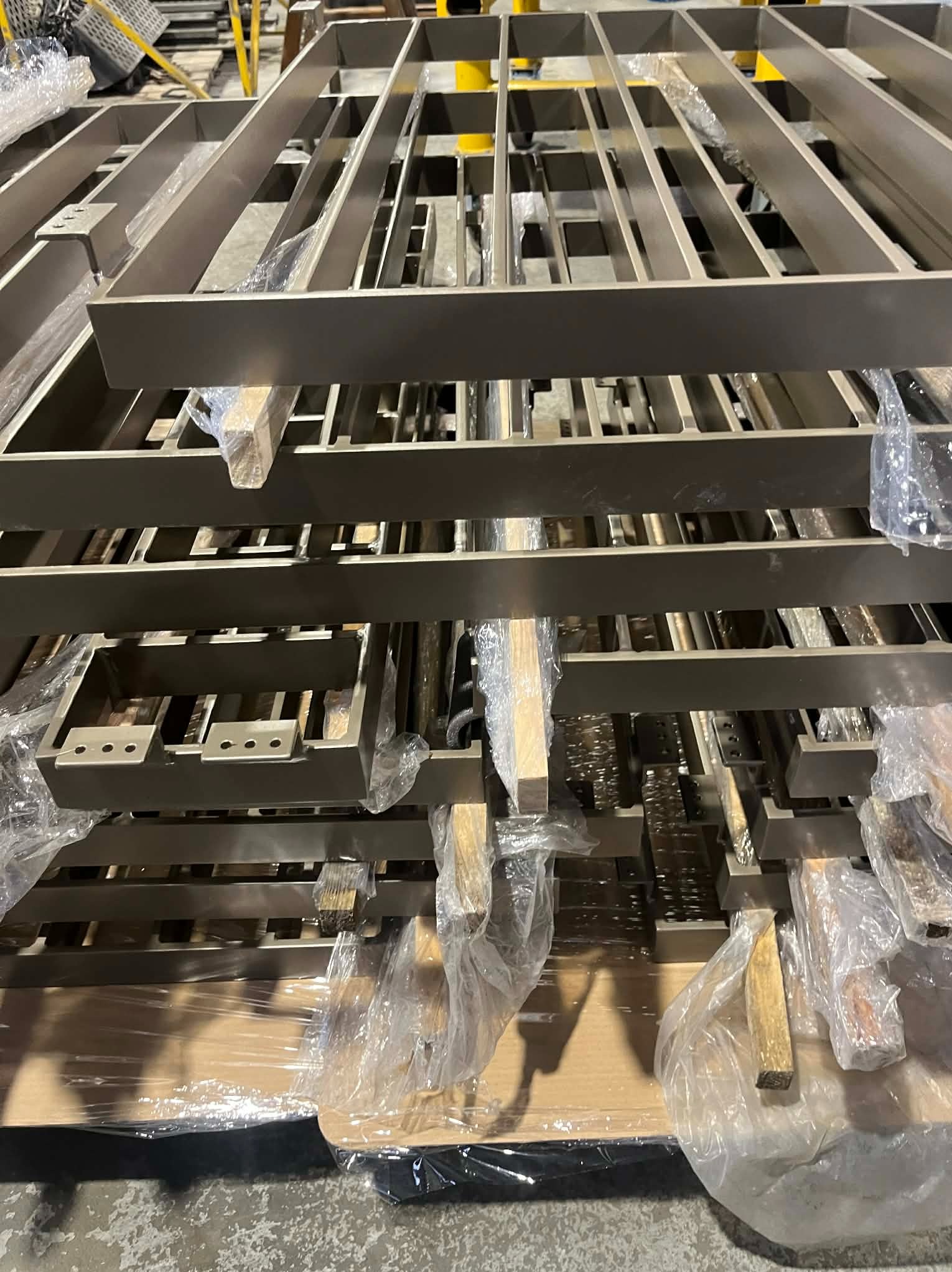 Stos metalowych elementów konstrukcyjnych, prawdopodobnie balustrad lub ogrodzeń, zabezpieczonych folią i drewnianymi przekładkami, gotowych do transportu lub montażu.