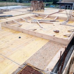 Szymon Makowiecki - Szczegółowy widok z góry na drewniany szalunek fundamentów z ceglanymi elementami i wystającymi prętami zbrojeniowymi, przygotowany do zalania betonem.