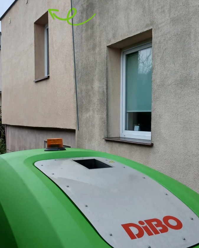 Elewacja budynku przed czyszczeniem, widoczne zabrudzenia. Na pierwszym planie urządzenie czyszczące Dibo. W tle okna i fragment dachu sąsiedniego budynku.