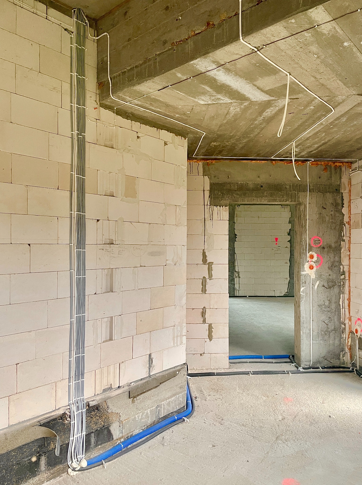 Surowy stan: wiązka kabli elektrycznych pionowo na ścianie z betonu komórkowego, rury instalacyjne w podłodze, widok wnętrza w trakcie budowy.