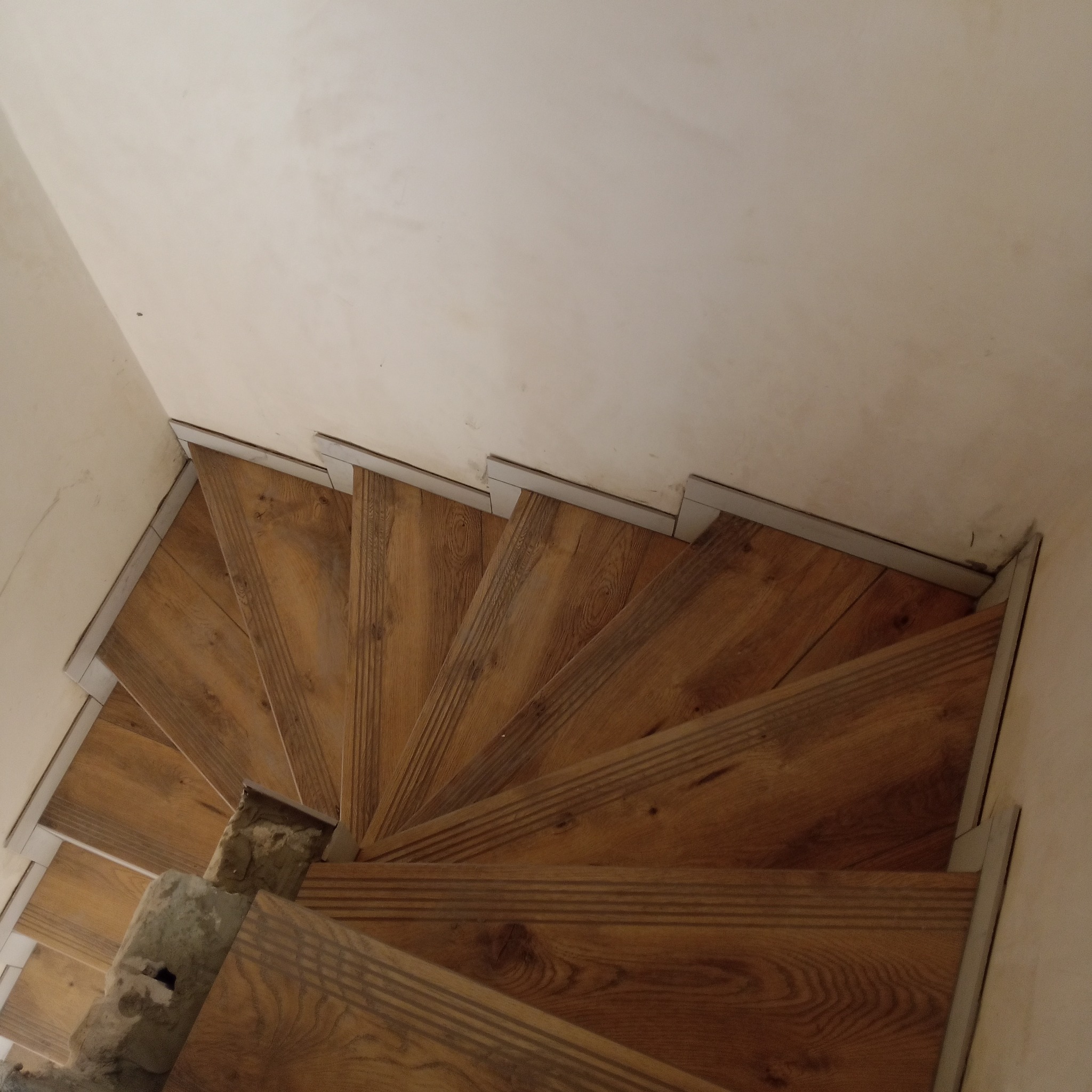 Drewniane schody spiralne z metalowymi listwami wykończeniowymi, widok z góry, jasne ściany w tle. Wykończenie schodów z dbałością o detale.