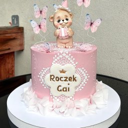 Iwona Korba - Różowy tort na roczek z misiem w czapeczce i motylami, dekorowany białymi koronkami i napisem 'Roczek Gai'. Uroczy i słodki wypiek na pierwsze urodziny.