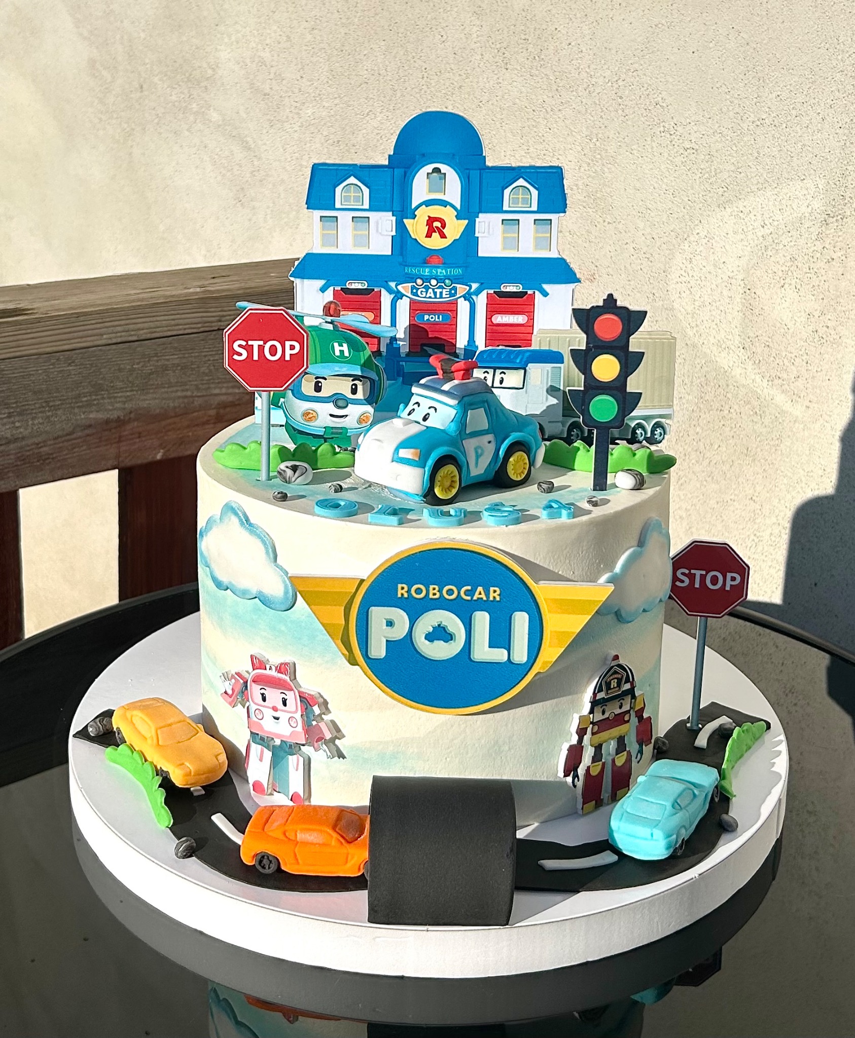Tort urodzinowy z motywem Robocar Poli: budynek stacji ratunkowej, figurki aut i znaków drogowych. Dekoracja z chmurkami i imitacją drogi.