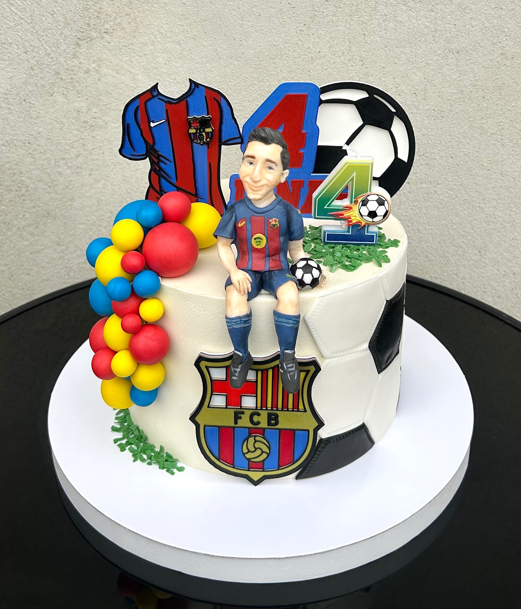 Tort urodzinowy w stylu piłkarskim z figurką zawodnika, koszulką FC Barcelony i liczbą 4, na białym talerzu.