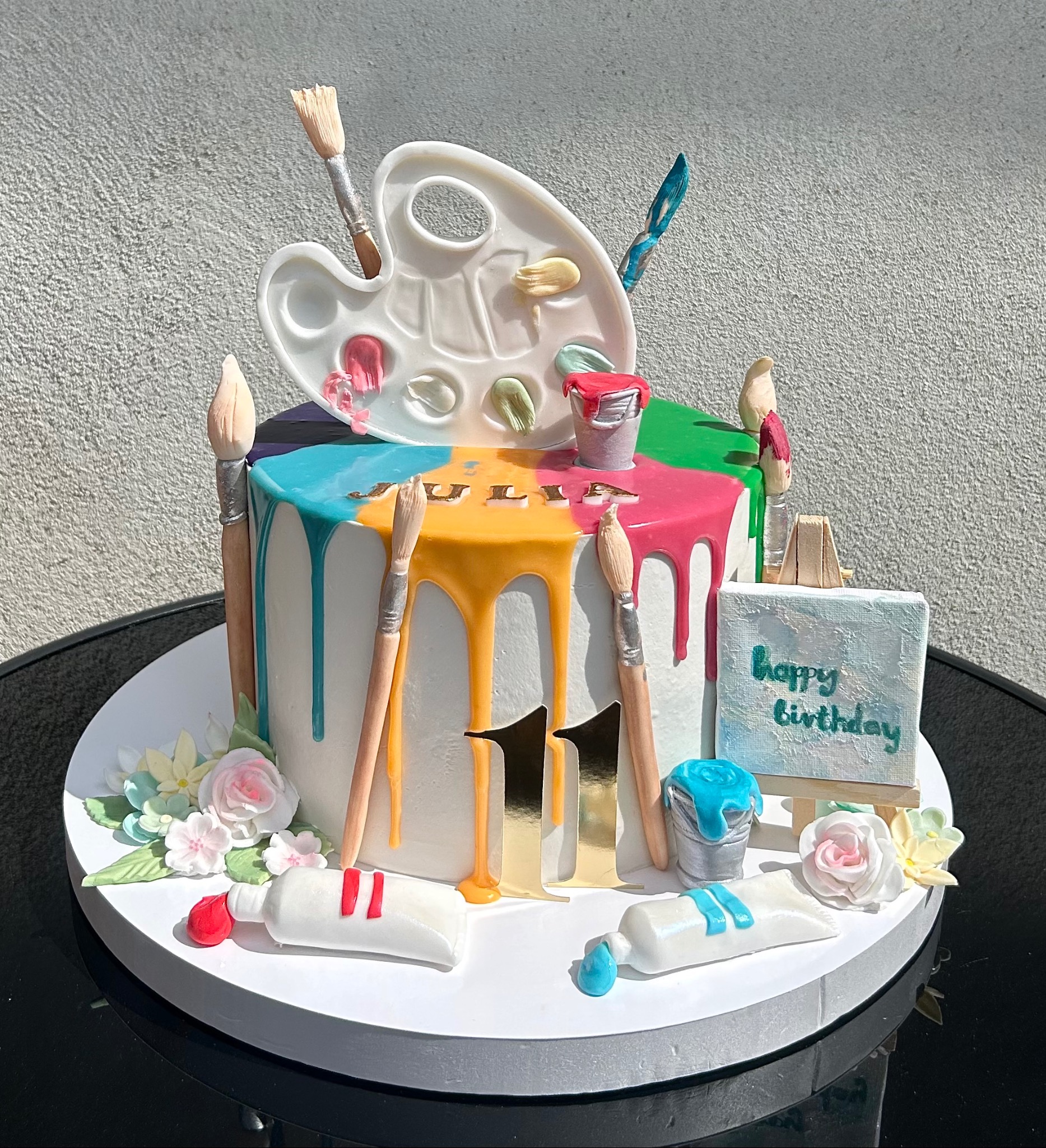 Artystyczny tort urodzinowy z paletą, pędzlami i farbami, zdobiony kolorowymi polewami i napisem 'Happy Birthday'. Idealny na 11 urodziny Julii.
