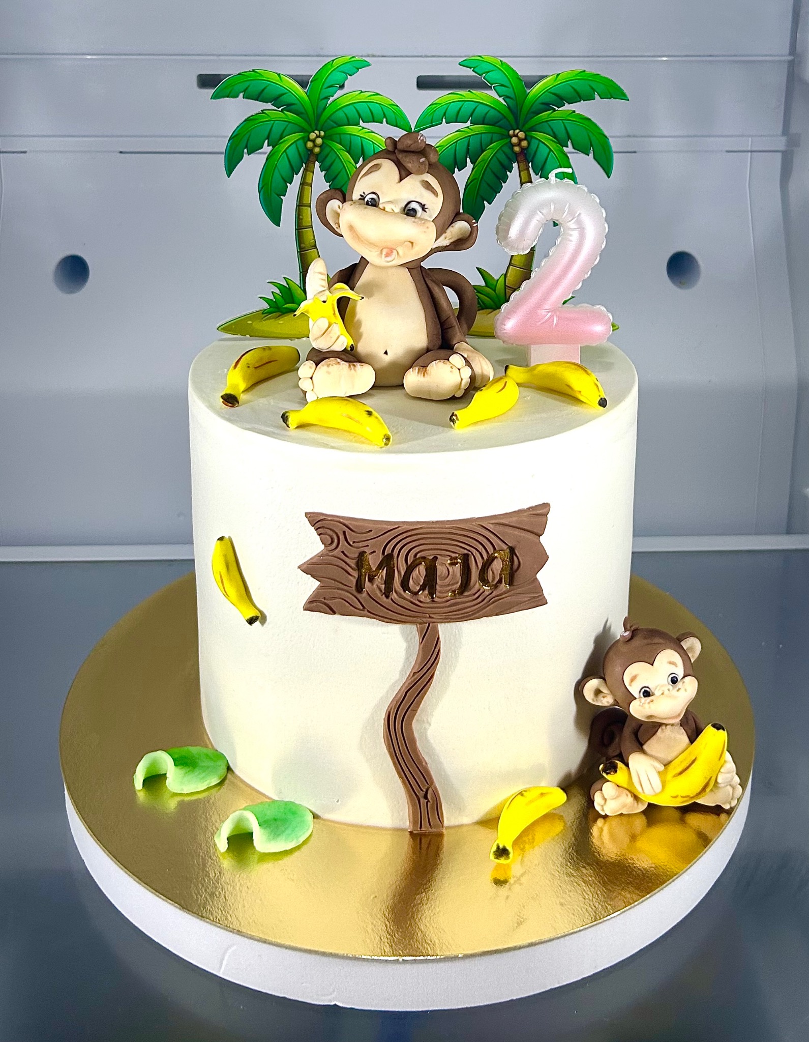 Tort urodzinowy z motywem małpki i bananów, dekorowany imieniem 'Maja' i cyfrą '2', wykonany w Ruszowie. Kremowy tort na złotej podkładce.