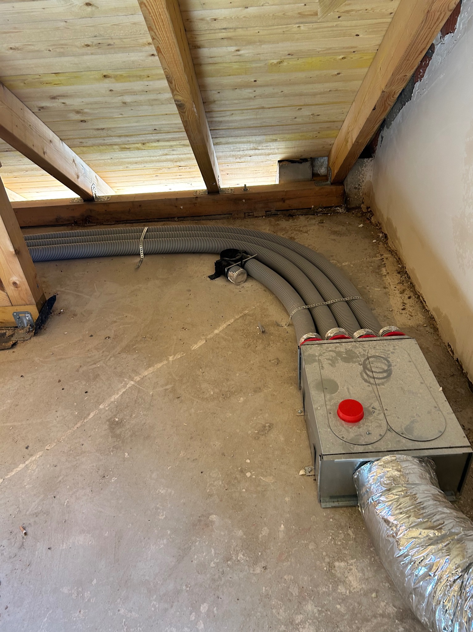 Szare, elastyczne rury wentylacyjne przymocowane do metalowej skrzynki z czerwonymi pokrywami, zamontowane na poddaszu z drewnianą konstrukcją dachu.