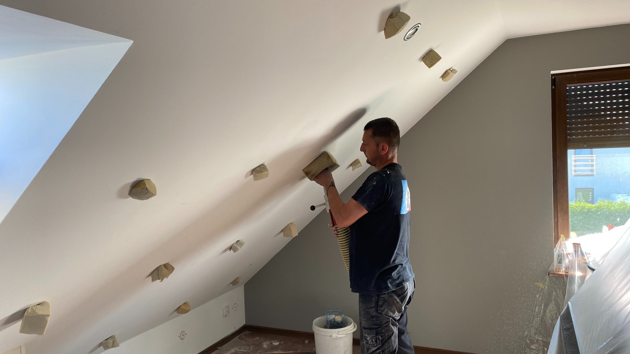 Pracownik aplikuje pianę montażową w szczeliny poddasza, przygotowując je do izolacji. Widoczne zabezpieczenia i narzędzia pracy.