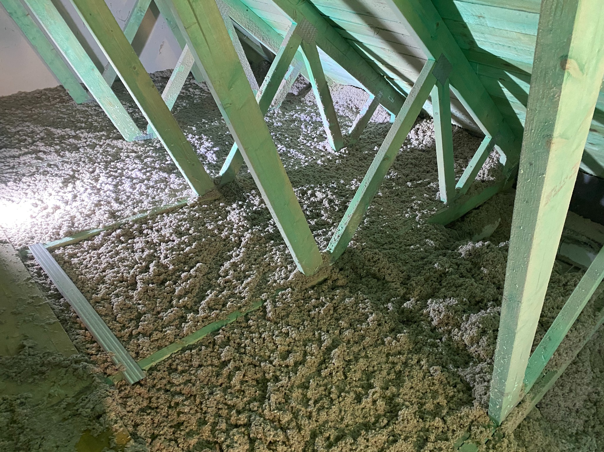 Poddasze po izolacji celulozą w Wysokiej Kamieńskiej. Widoczne zielone krokwie i wypełnienie przestrzeni materiałem izolacyjnym. Detal z bliska.