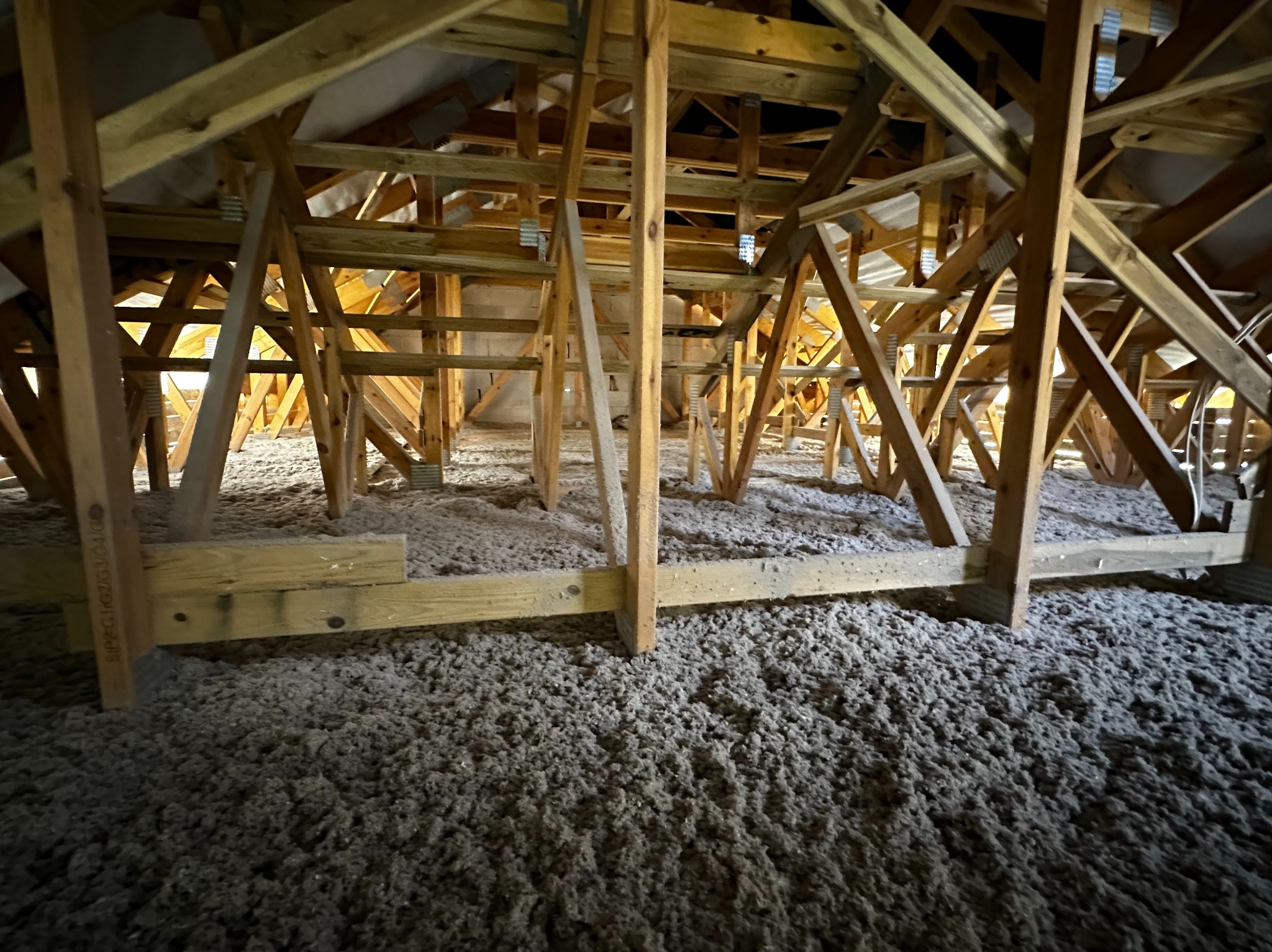 Poddasze z drewnianą konstrukcją wypełnione szarą wełną mineralną, widok z dołu, oświetlenie punktowe. Izolacja termiczna poddasza.