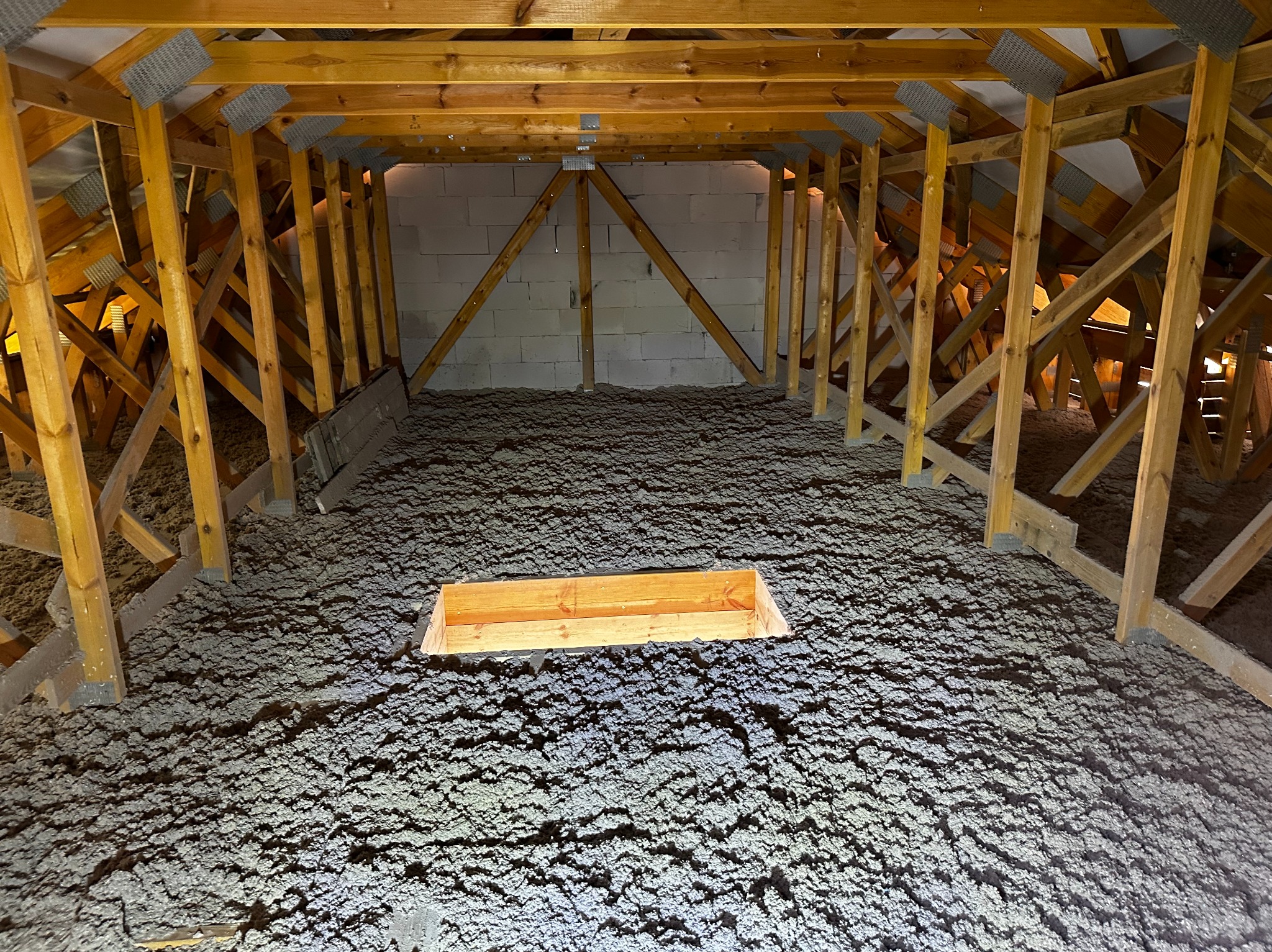 Poddasze z drewnianą konstrukcją i izolacją z wełny mineralnej, widoczny otwór rewizyjny. Ściana szczytowa z bloczków betonowych.