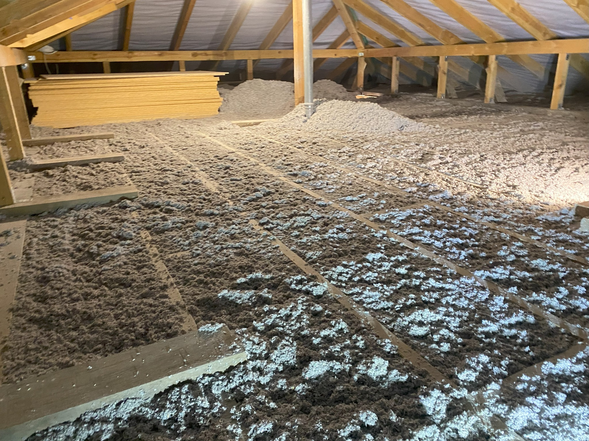 Poddasze z widoczną izolacją z wełny mineralnej, drewnianą konstrukcją dachu i stertą płyt OSB w rogu. Widok z góry na ocieplony strych.