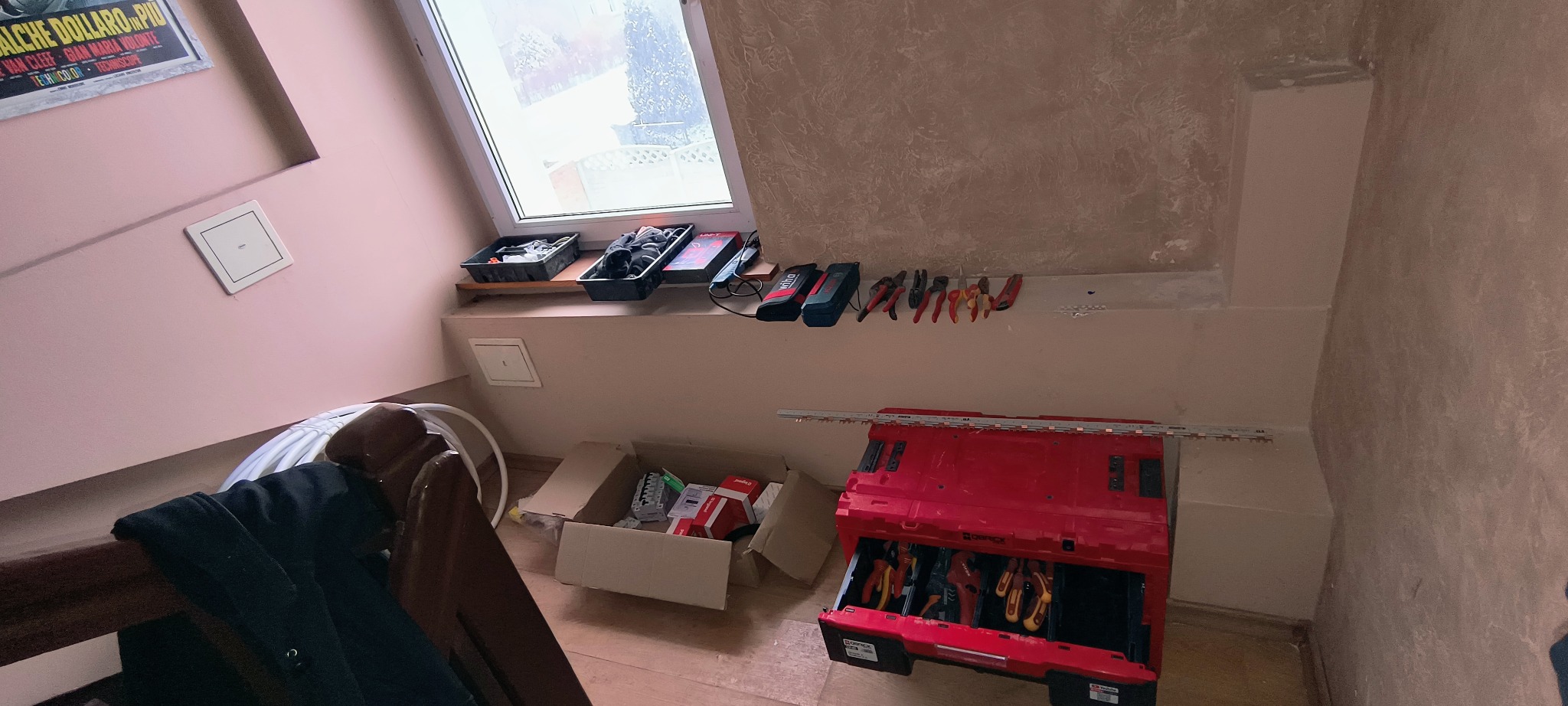 Rozłożona skrzynka narzędziowa z zestawem szczypiec i wkrętaków, obok okna dachowego z widocznymi narzędziami i akcesoriami elektrycznymi.