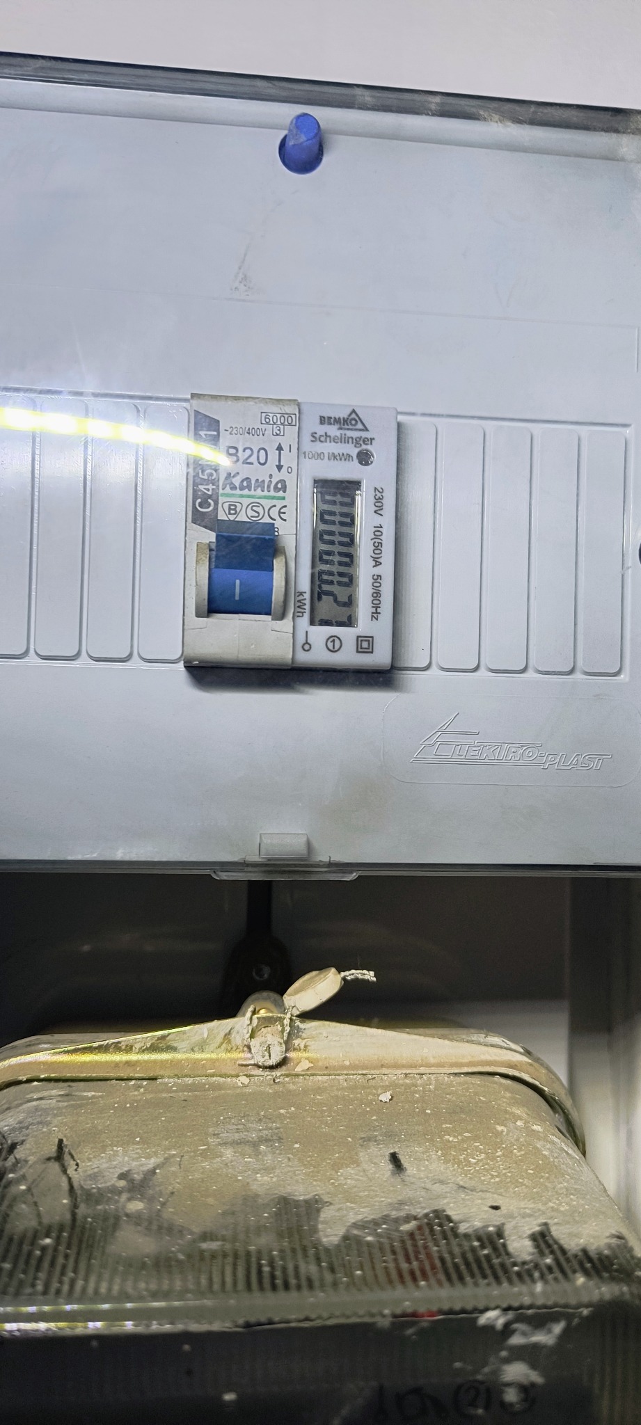 Szczegółowe ujęcie licznika elektrycznego Bemko Schelinger w szarej obudowie Elektro-Plast, z widocznym bezpiecznikiem Kania C45 B20 i wskazaniem 00000.2 kWh.