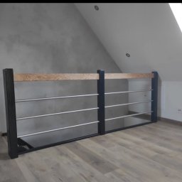 Kamil jonca - Nowoczesna balustrada z czarnymi słupkami, drewnianą górną belką i metalowymi prętami, zamontowana w jasnym wnętrzu poddasza z drewnianą podłogą.
