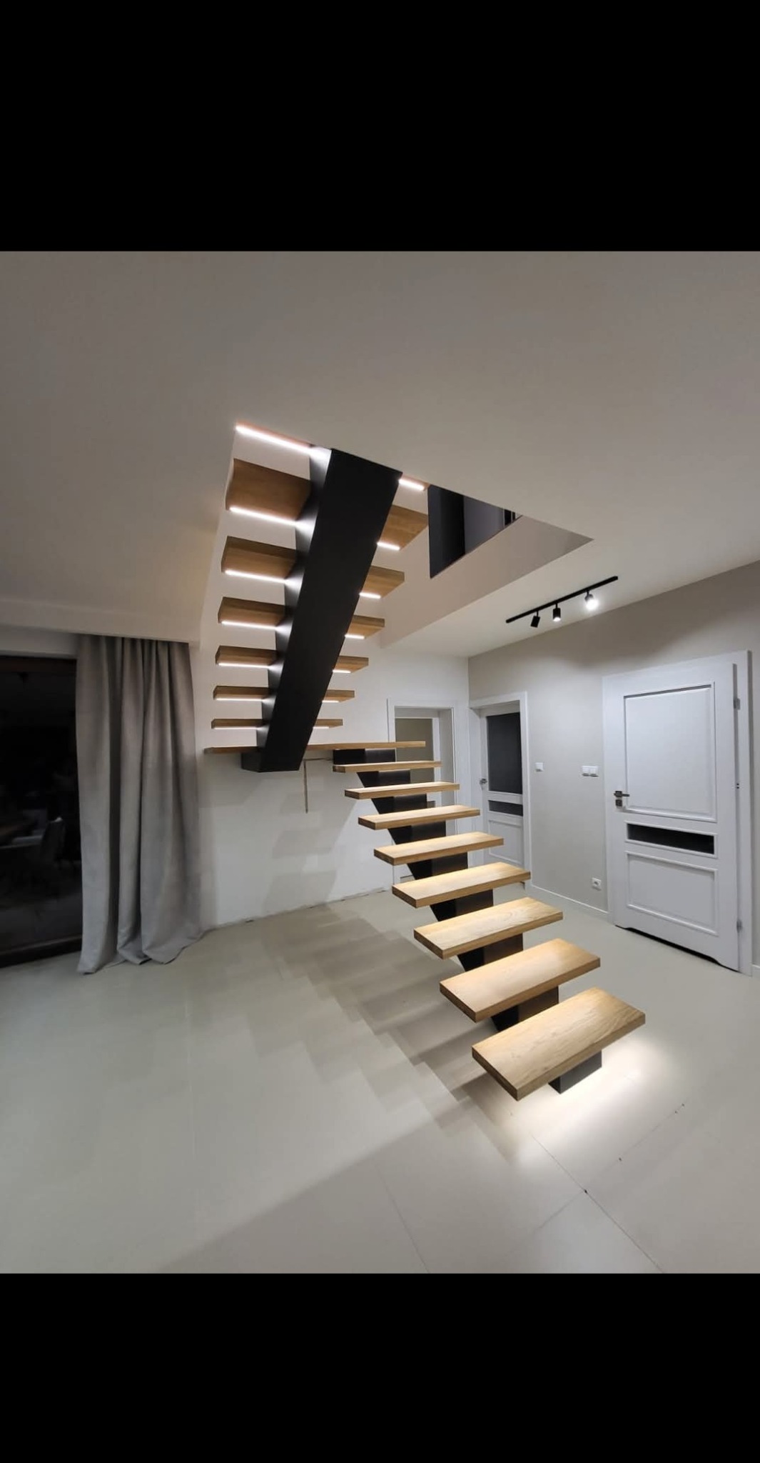 Nowoczesne schody drewniane z podświetleniem LED, wspornikowe stopnie i czarna konstrukcja nośna. Minimalistyczny design w jasnym wnętrzu.