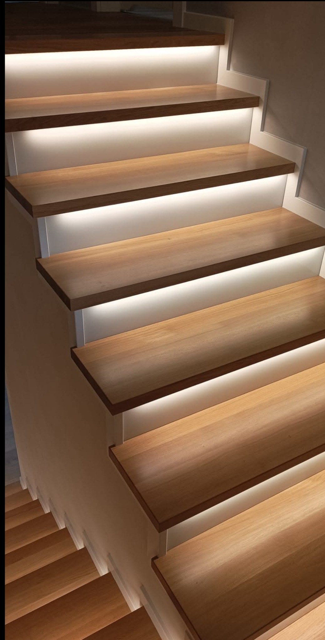Nowoczesne schody z drewna z subtelnym podświetleniem LED, widok z góry, ukazujący detale wykończenia i ciepłe światło. Minimalistyczny design.