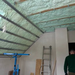 BIRTECH JAKUB BIR - Poddasze w Kartuzach po natrysku pianki PUR, widoczne metalowe profile i drabina. Izolacja termiczna wykonana z dbałością o detale, równomierna struktura piany.