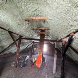 BIRTECH JAKUB BIR - Poddasze po ociepleniu pianką PUR, widoczne drewniane elementy konstrukcyjne i warstwa izolacji. Na podłodze narzędzia i worki. Światło wpada przez okno.