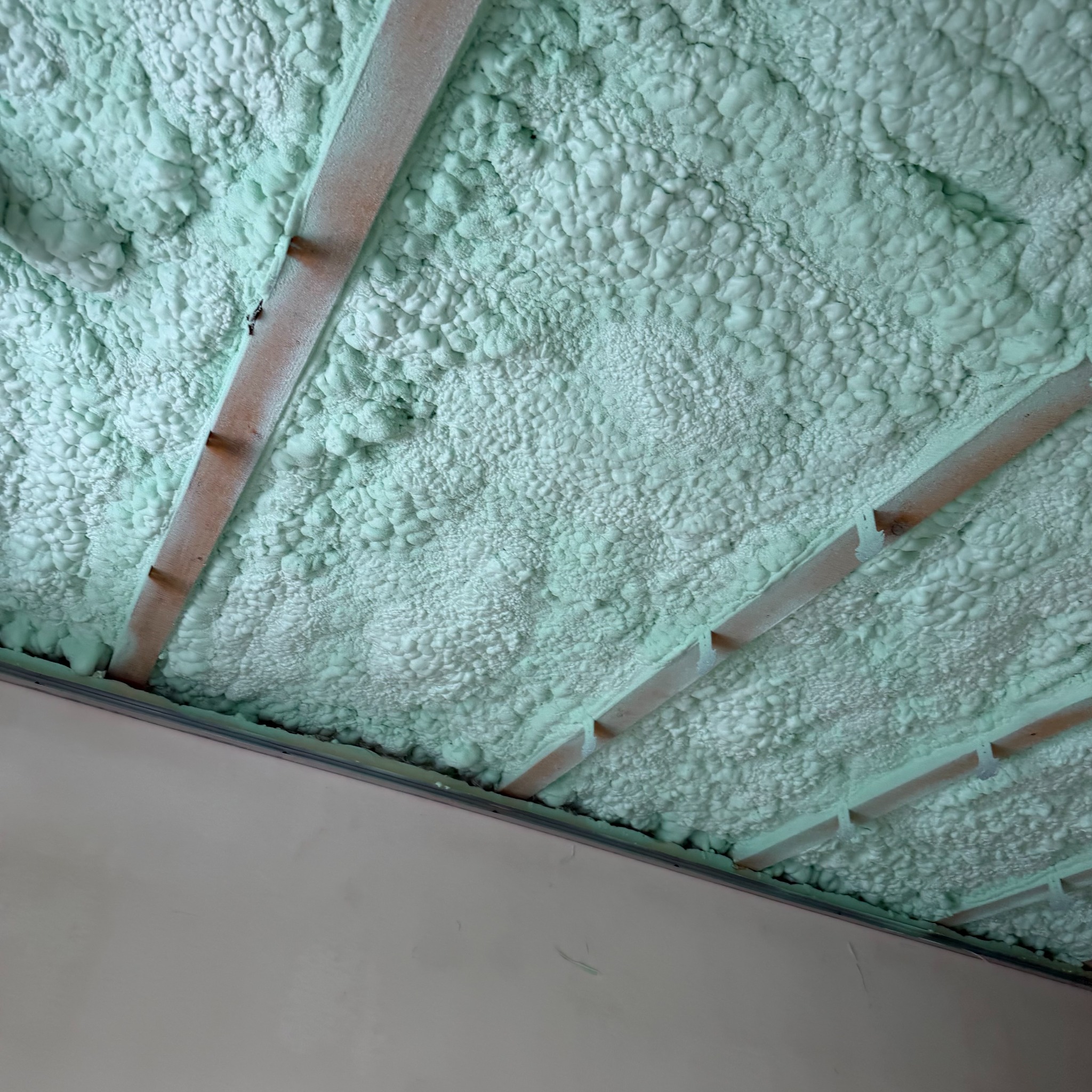 Poddasze ocieplone pianką PUR w kolorze jasnozielonym, widoczne drewniane elementy konstrukcji dachu. Aplikacja pianki wykonana precyzyjnie, wypełniając całą przestrzeń.