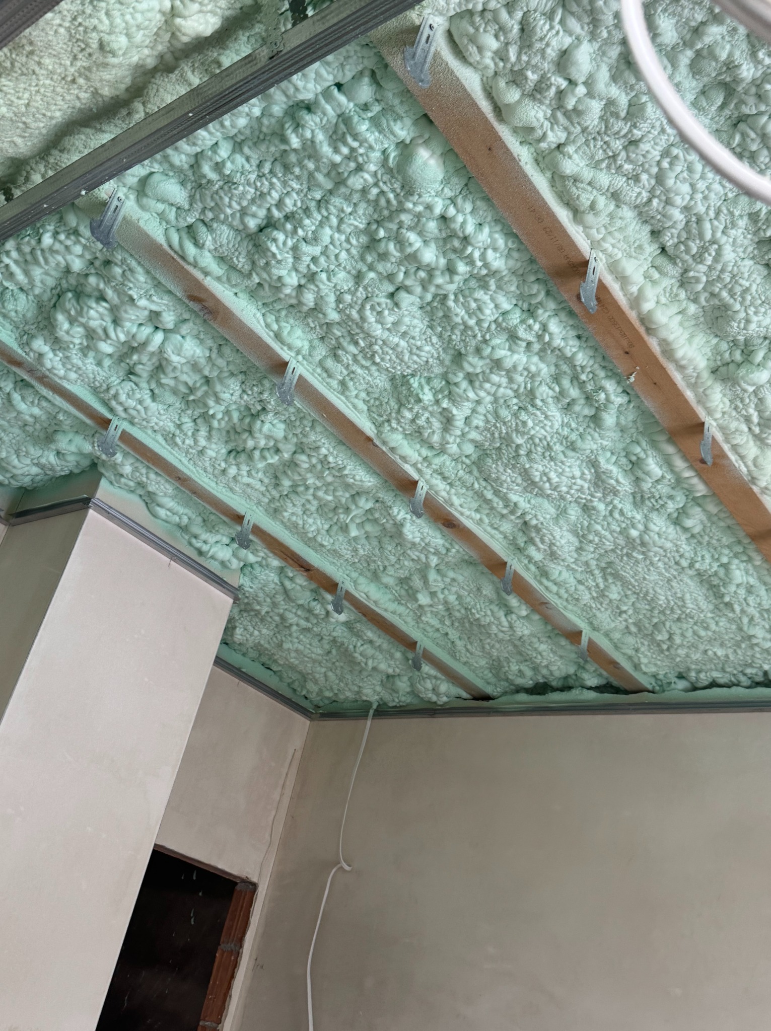 Poddasze po natrysku pianki PUR, widoczne drewniane belki i metalowe profile. Jasnozielona pianka szczelnie wypełnia przestrzeń, tworząc izolację termiczną.