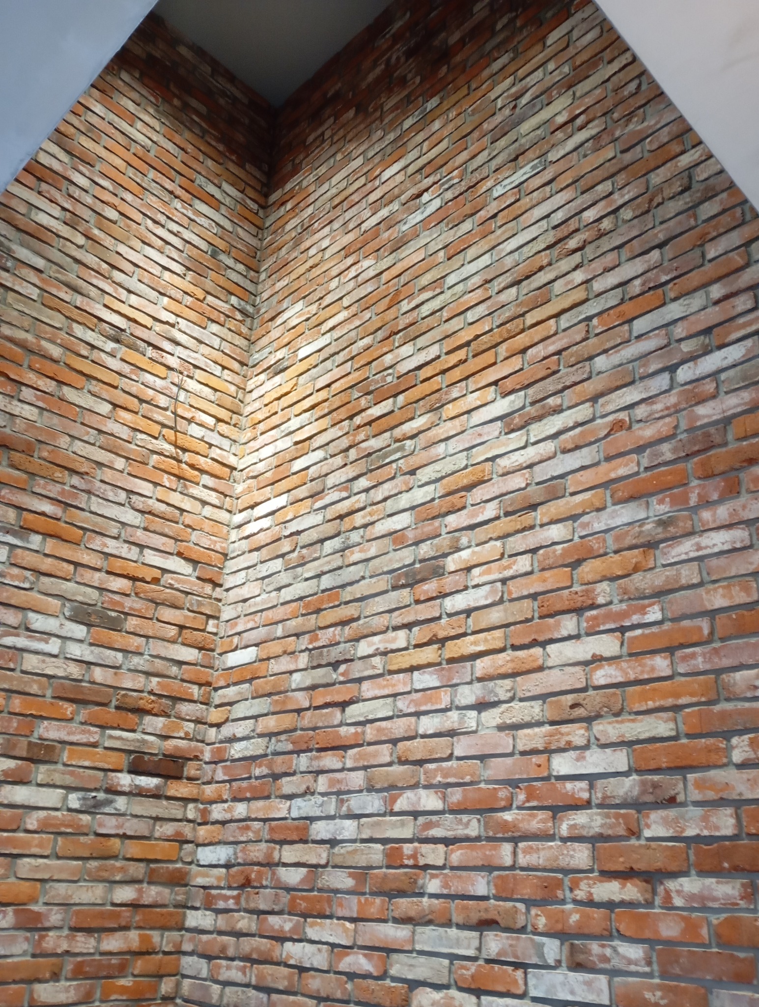 Dekoracyjna ściana z cegieł w odcieniach czerwieni i bieli, ułożonych w regularny wzór. Widoczny fragment łuku sufitowego.