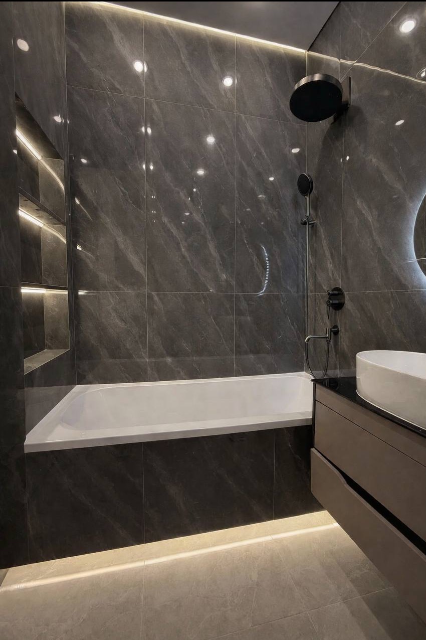 Nowoczesna łazienka z marmurowymi płytkami, podświetlaną wanną i półkami wnękowymi. Czarna armatura i okrągłe lustro z podświetleniem dodają elegancji.