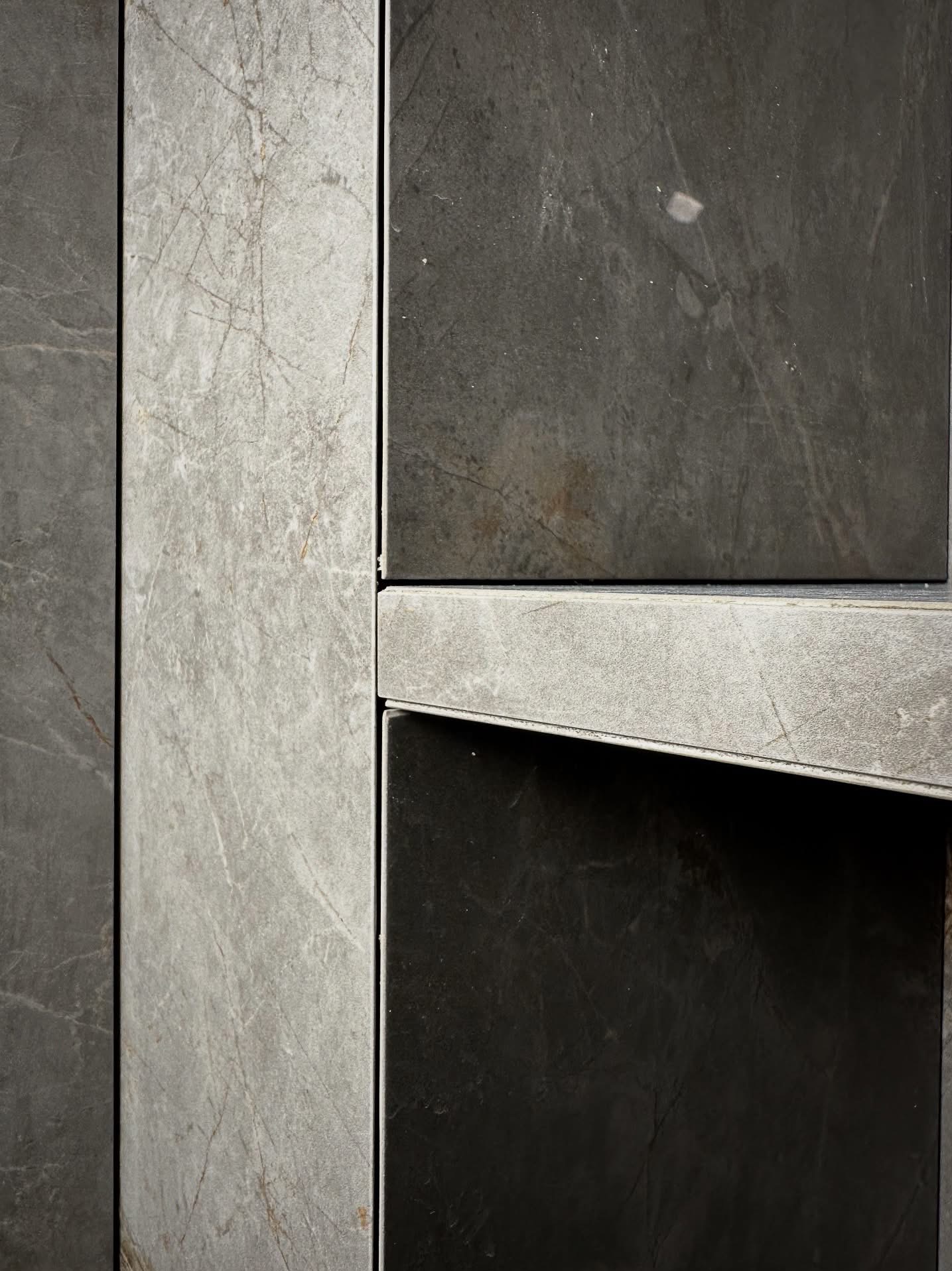 Szczegółowe ujęcie szarych płytek imitujących marmur, ułożonych w pionowe pasy z widocznymi fugami. Płytki w odcieniach szarości i grafitu, z delikatnymi żyłkami.