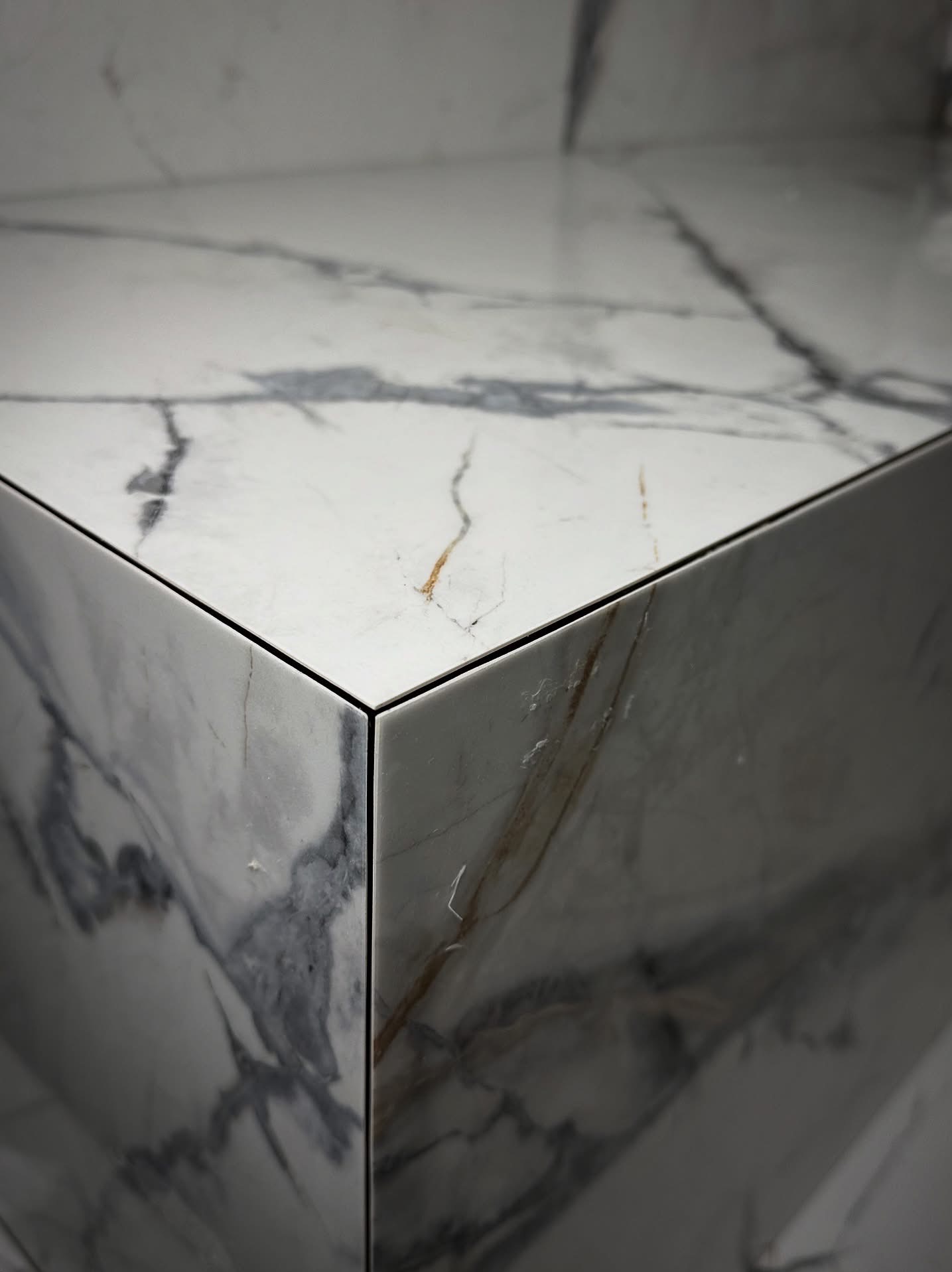 Detal narożnika wykończonego płytami z marmurowym wzorem. Precyzyjne łączenie płyt, widoczne subtelne żyłki i polerowana powierzchnia. Minimalistyczny design.