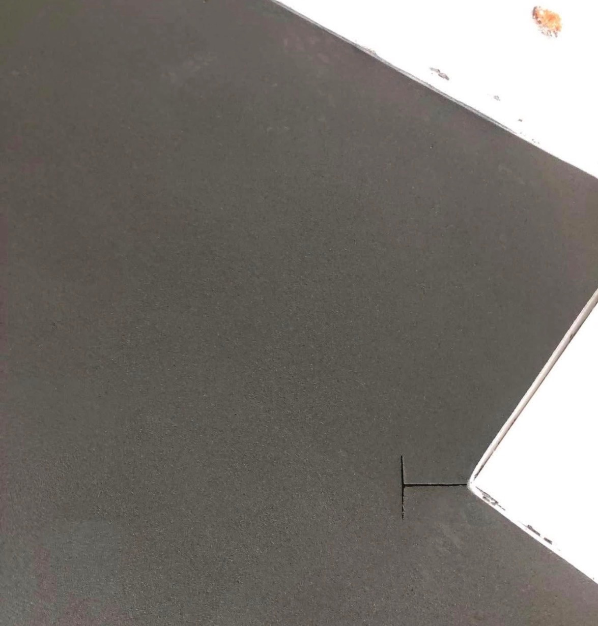 Gładka, szara powierzchnia z nacięciem dylatacyjnym przy białej krawędzi. Minimalistyczne ujęcie detalu posadzki.