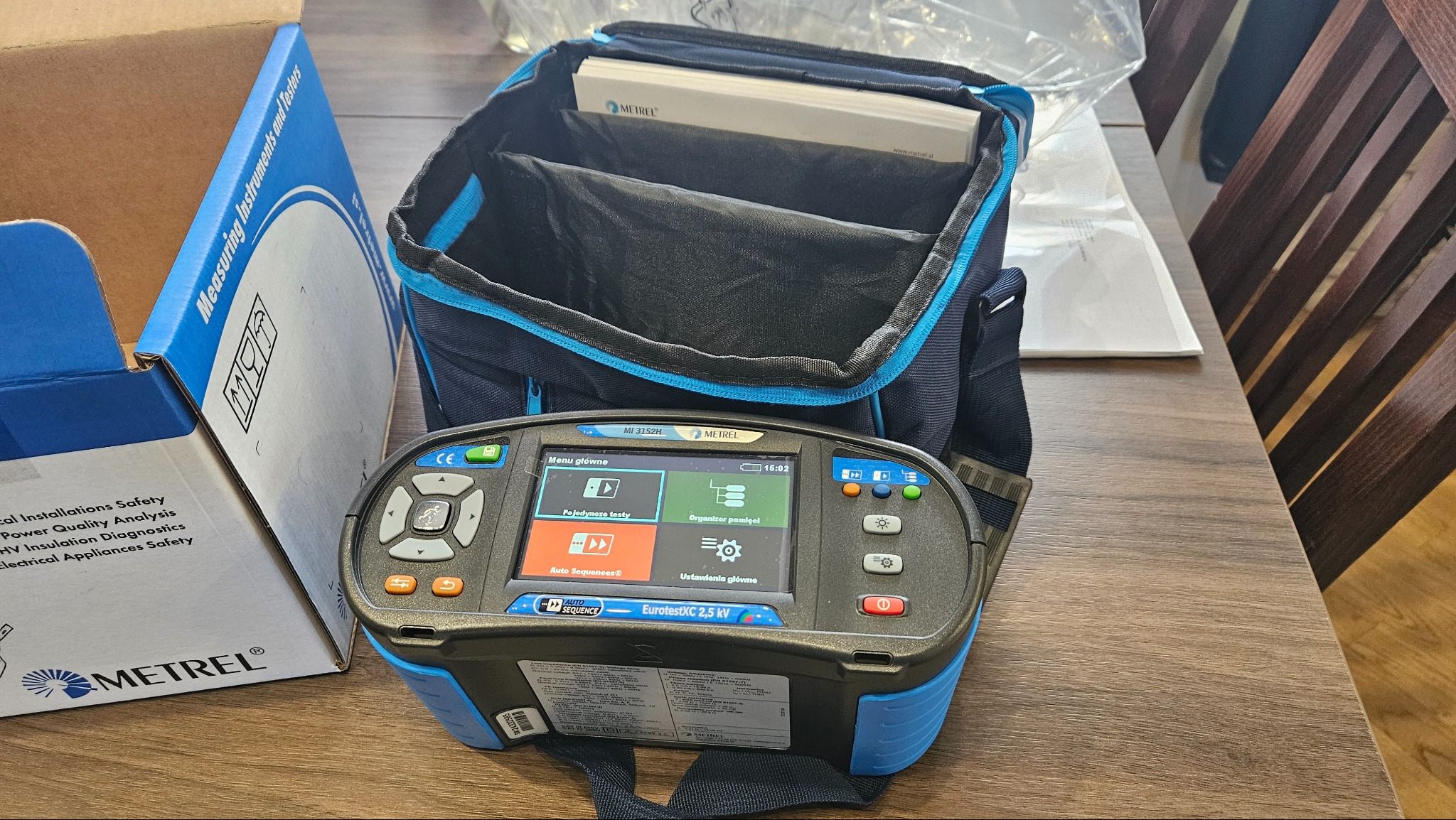 Profesjonalny miernik elektryczny Metrel EurotestXC 2,5 kV w torbie transportowej, obok pudełko z instrukcjami. Sprzęt do pomiarów instalacji elektrycznych.