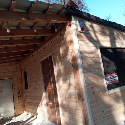 Usługi budowlane - Drewniana konstrukcja z widocznym zadaszeniem, oświetleniem i drzwiami. Na ścianie tabliczka informacyjna o ochronie obiektu. Widoczne elementy wykończeniowe.