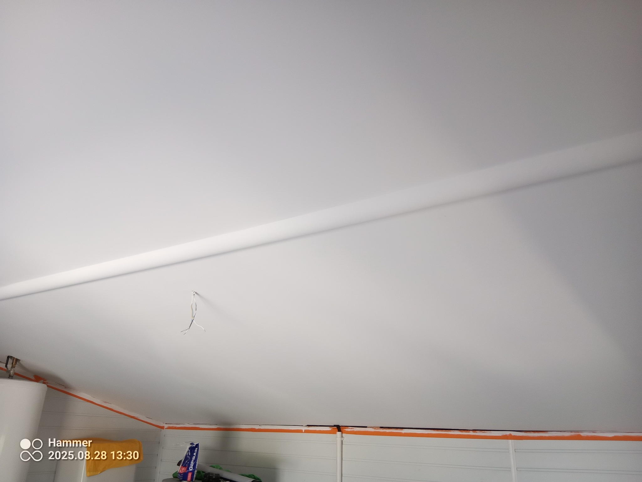 Biały sufit poddasza z widoczną listwą, wystającymi przewodami i fragmentem bojlera. Pomarańczowa taśma malarska zabezpiecza krawędzie. Widoczne panele ścienne.